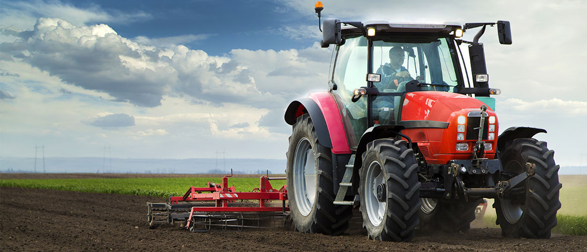 Red tractor with man driving through fields with tiller attachment behind