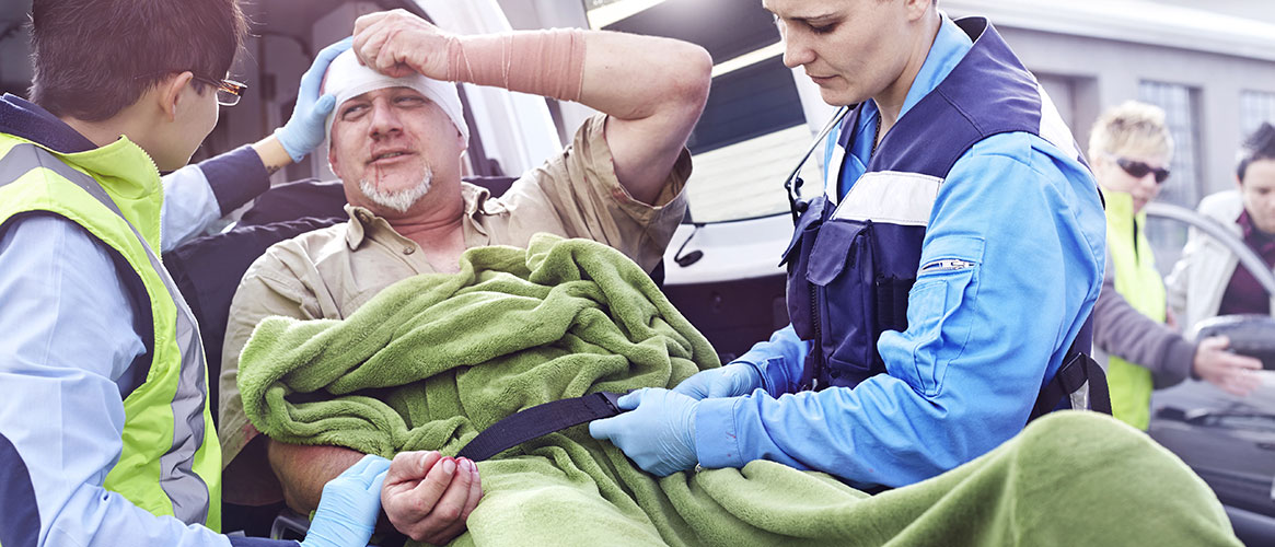 Rescue workers tending to car accident victim on stretcher at back of ambulance