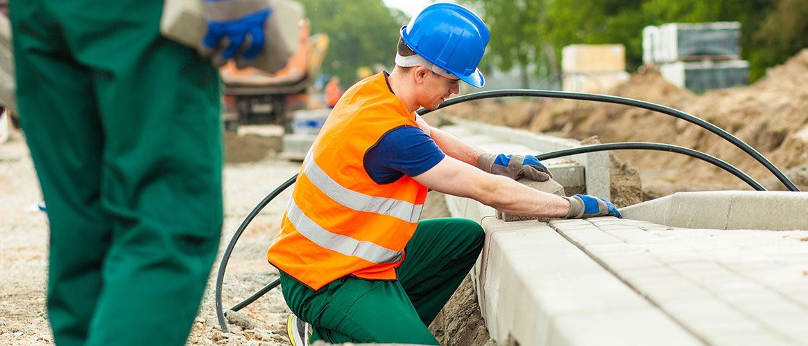 Brickworker kneeling to lay bricks on road side